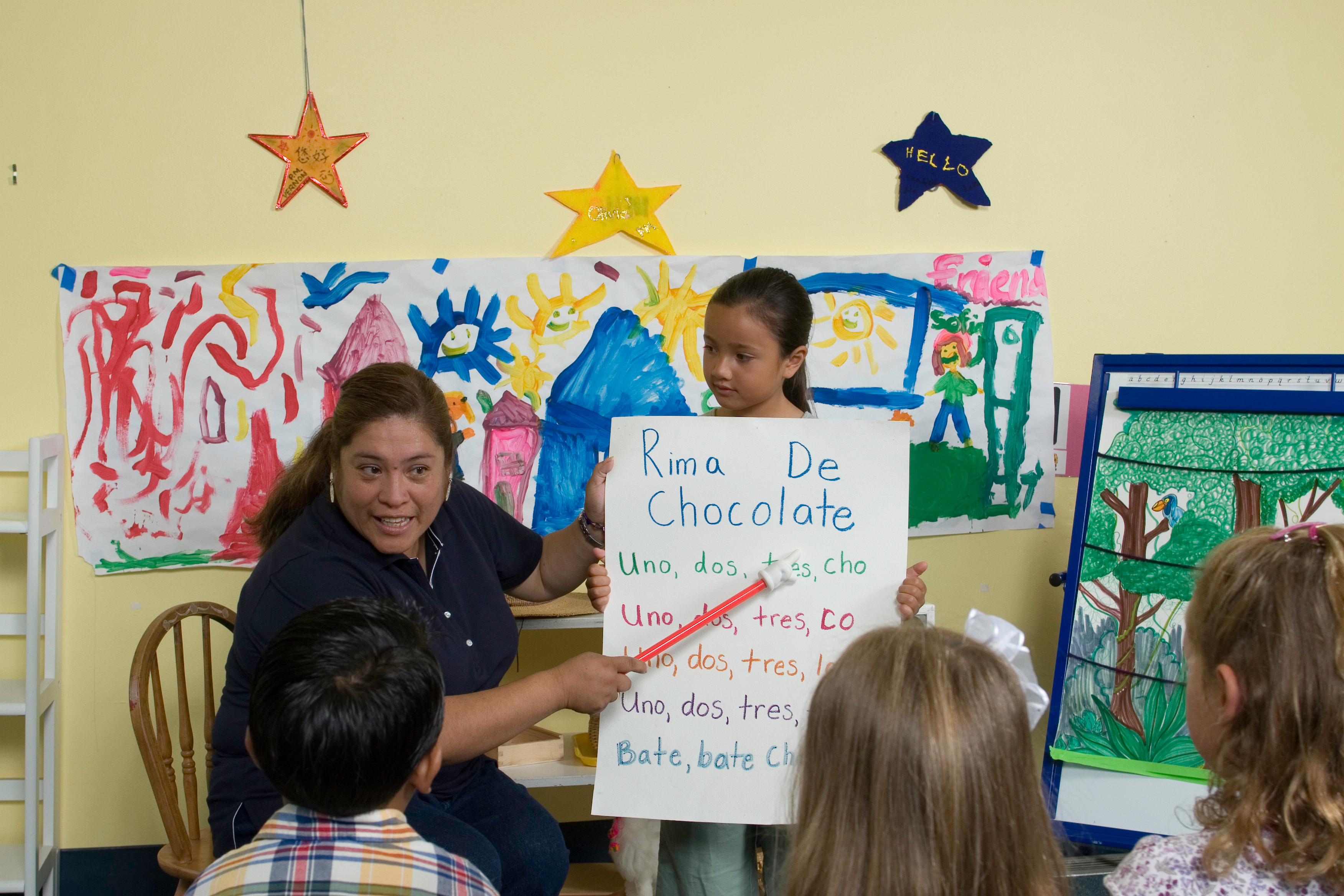 A kindergarten teacher uses a pointer to count while a student holds up the visual to the class