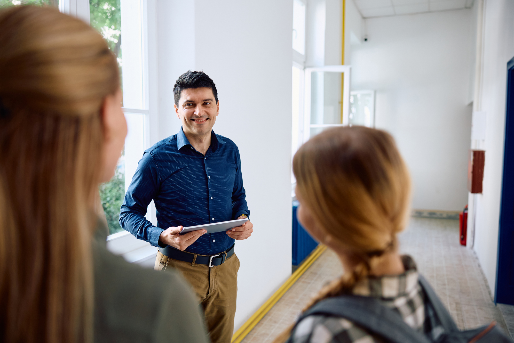 Happy middle school principal communicating with mother and her daughter in school hallway