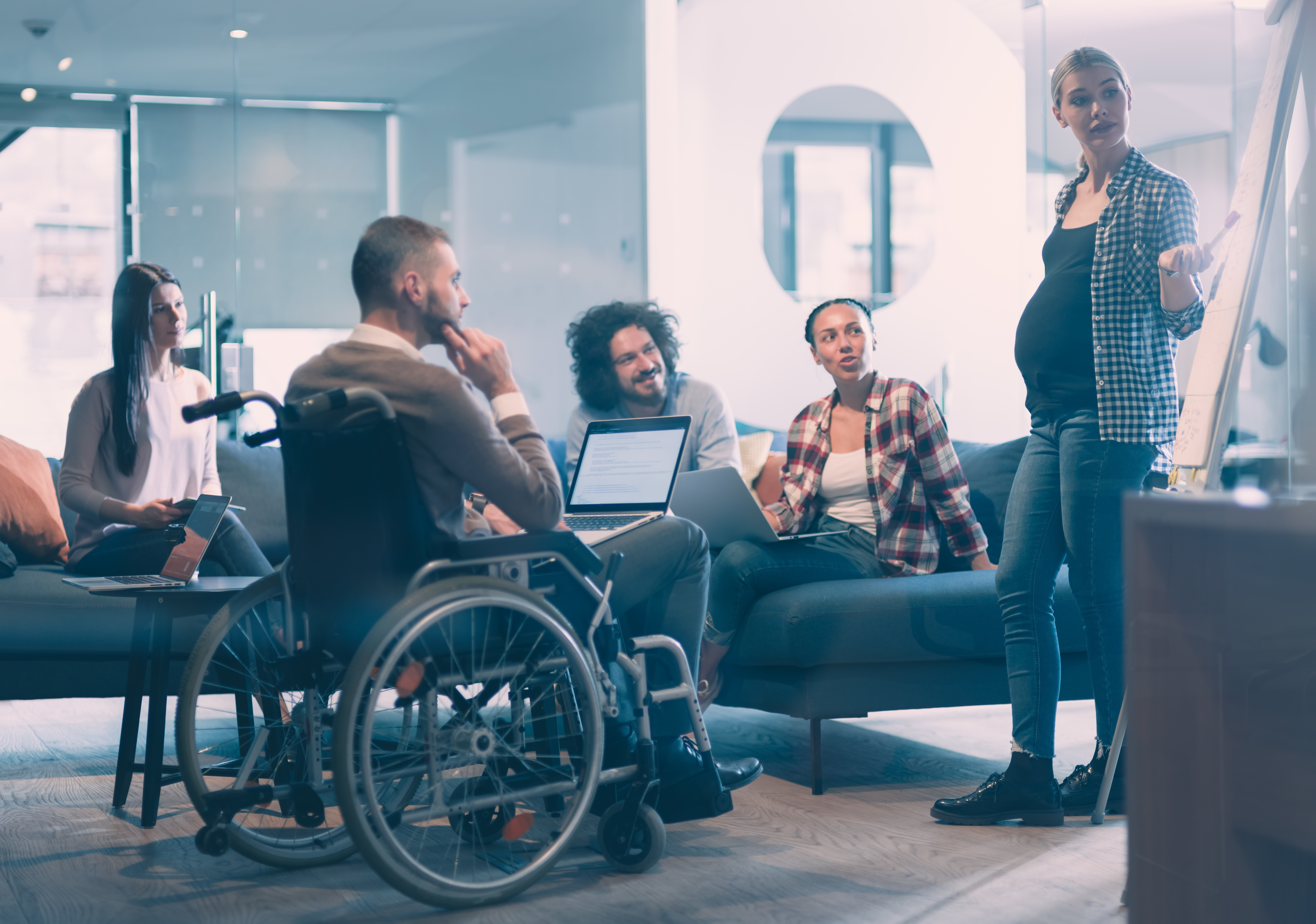 Pregnant woman leads diverse team meeting colleague in wheelchair participates