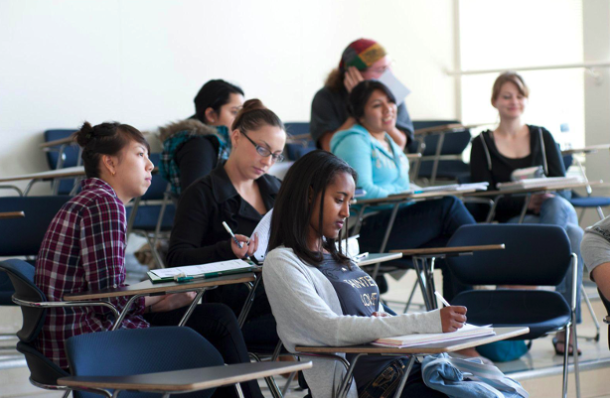 College students take notes at their desks in a classroom.