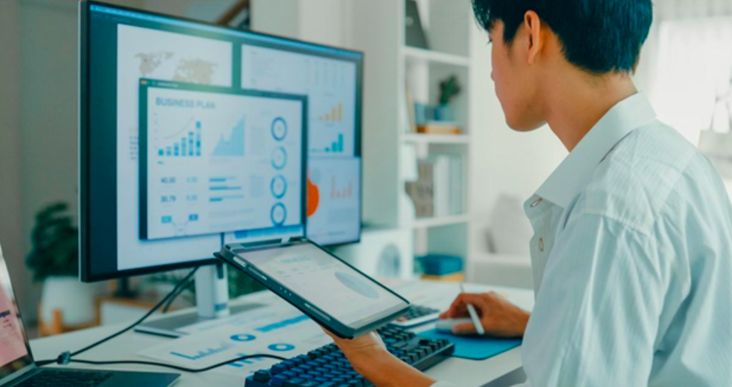 A businessperson uses a desktop computer and a tablet to develop a business plan.