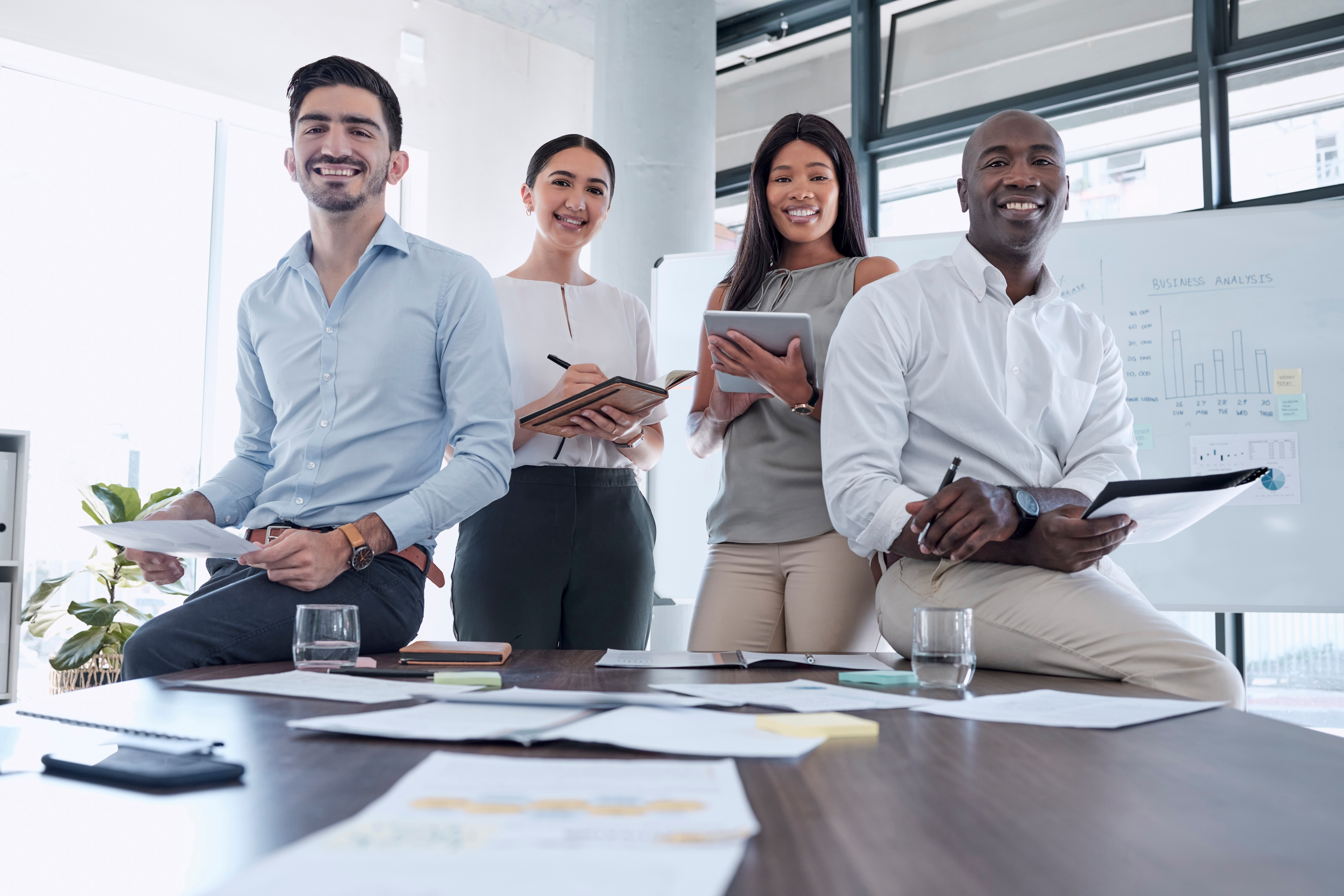 A diverse group of business professionals in a conference room smile at the camera.