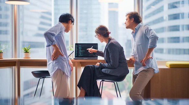 Three business professionals work on a computer.