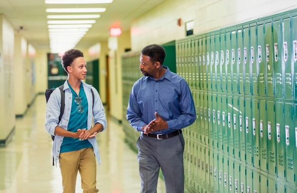 A high school administrator talks with a student in a school hallway.