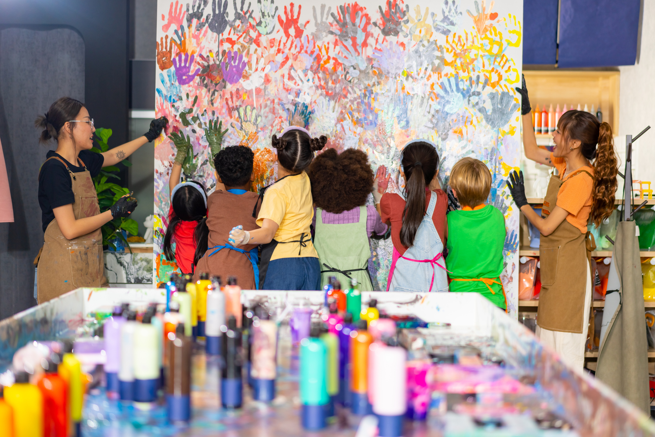 Art teachers watch as students place their painted hands on the canvas to leave their handprints