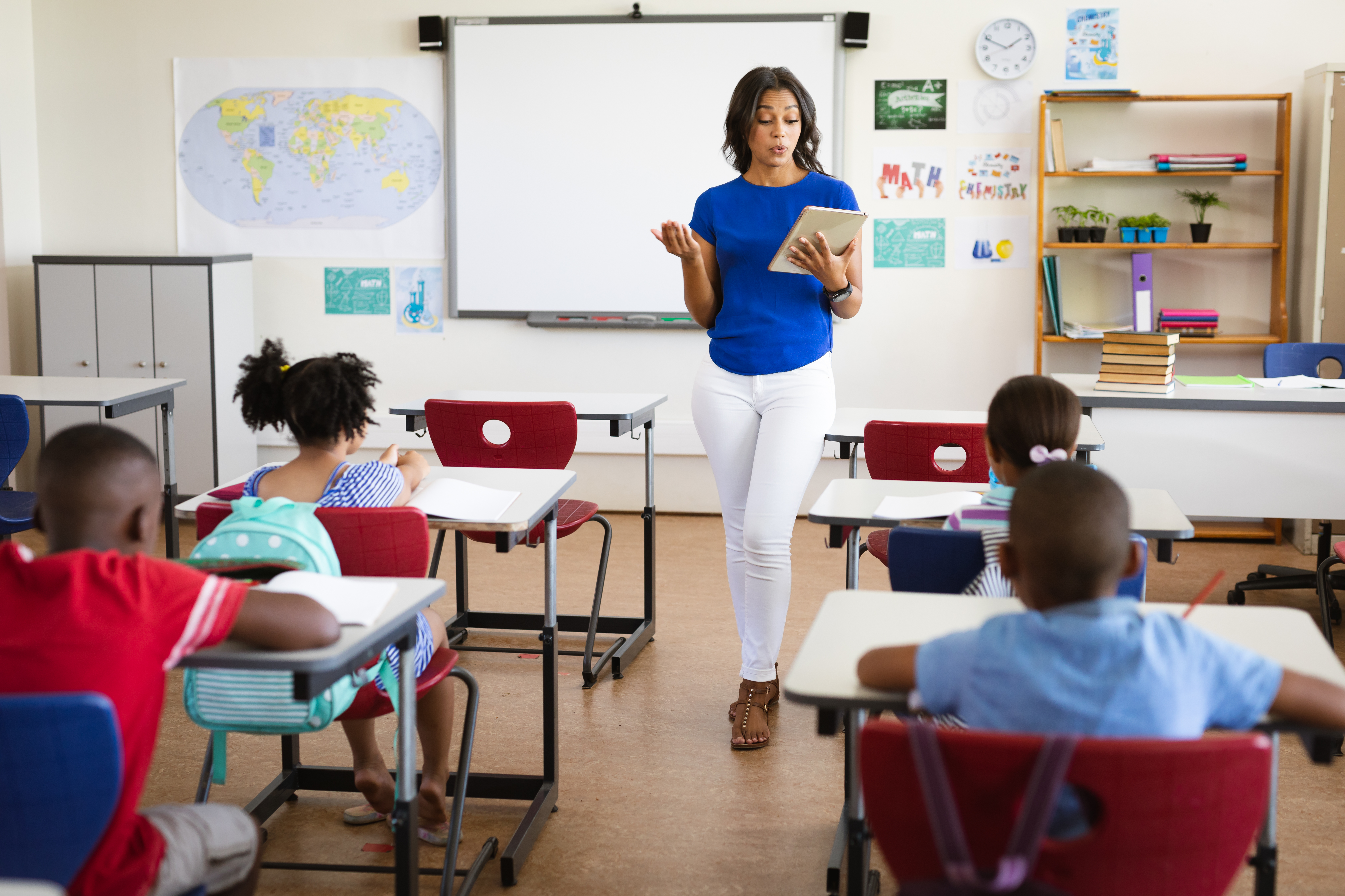 Female teacher with digital tablet teaching class elementary school.