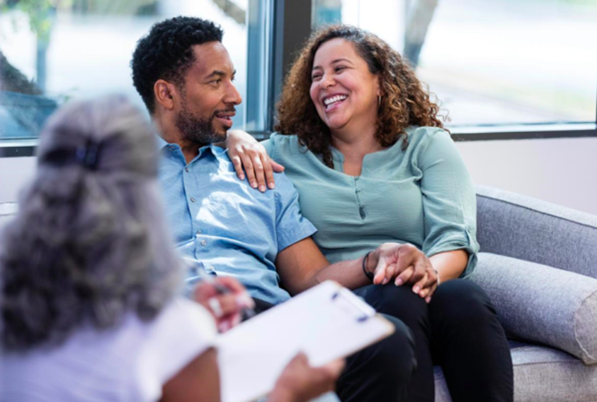 A happy and laughing couple seated in their marriage and family therapists office