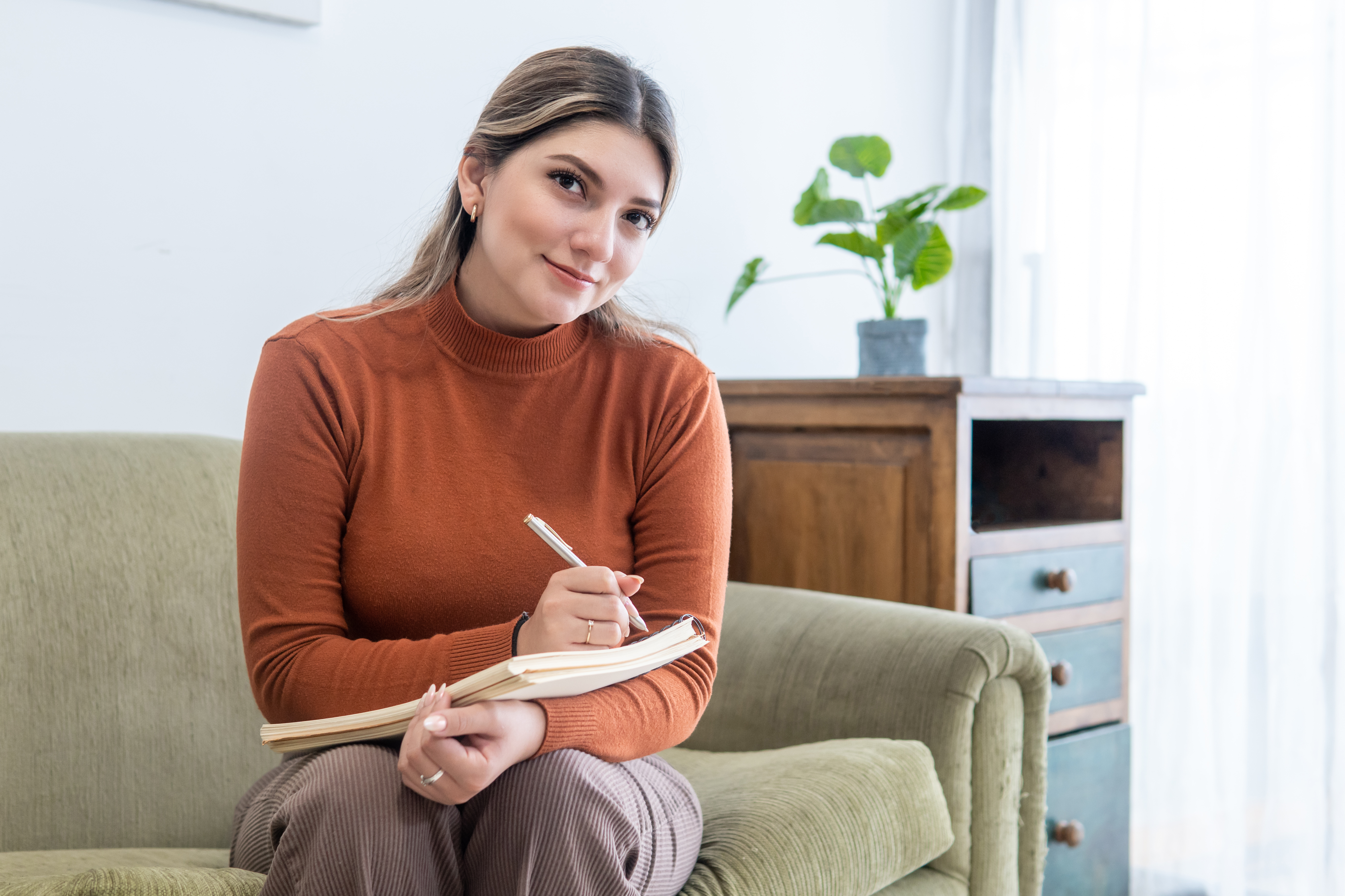 A young Latinx psychologist smiles at the camera while seated in their office