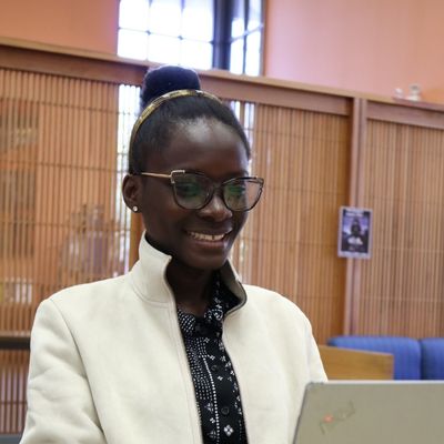 A student smiling, sitting at a table, and typing on a laptop.