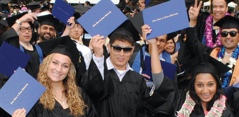 Students in caps and gowns at graduation holding up their diplomas.