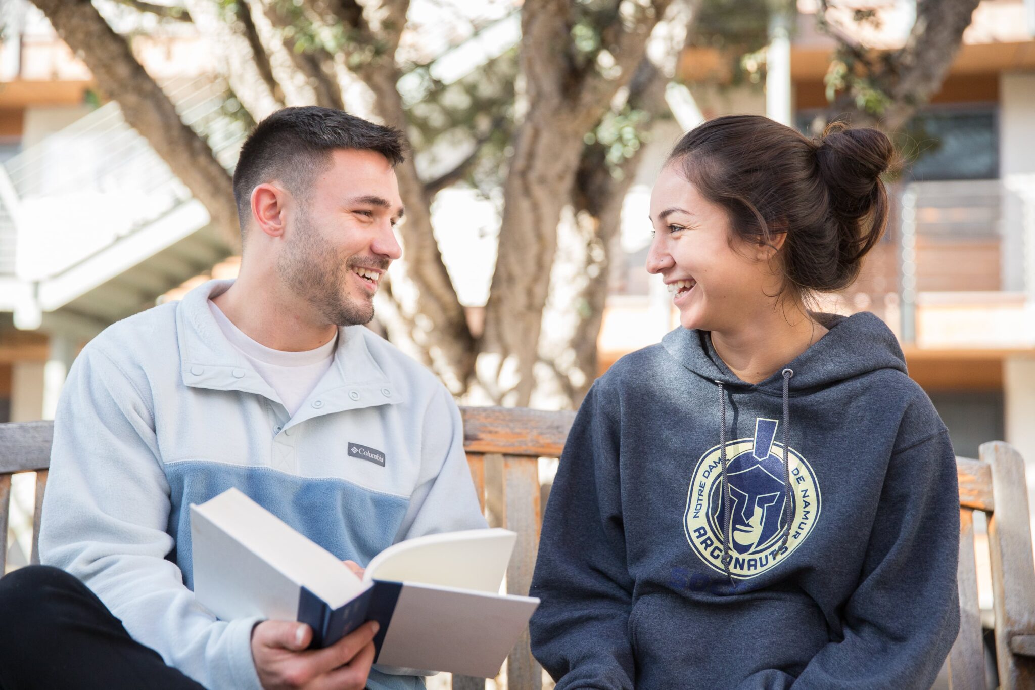 two students sitting on bench with book