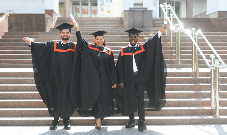 students standing in front of stairs holding diplomas